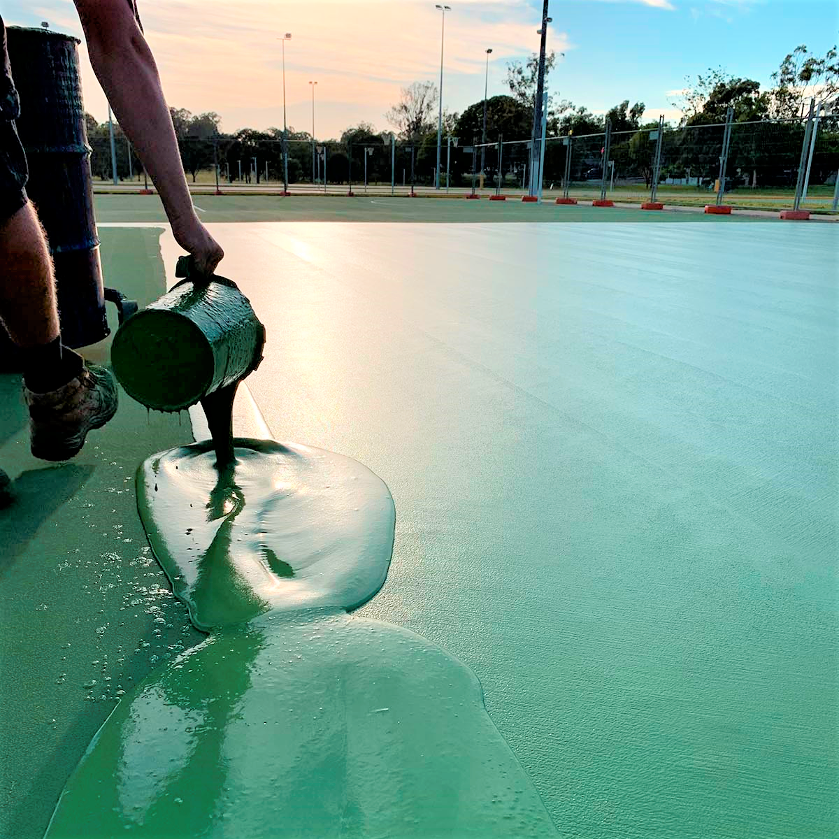 Trabajador vertiendo revestimiento de PU de silicona verde, destacando el flujo suave y la aplicaci&oacute;n perfecta para las canchas.